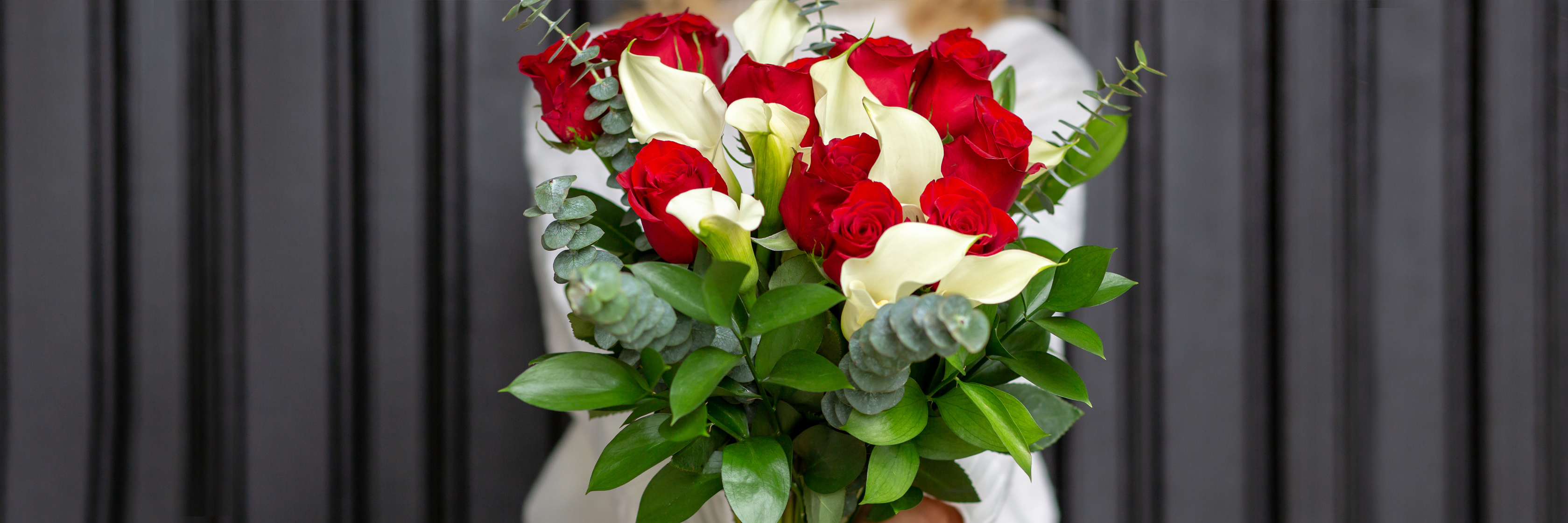 A vibrant bouquet featuring red roses and white calla lilies, elegantly arranged with lush greenery.