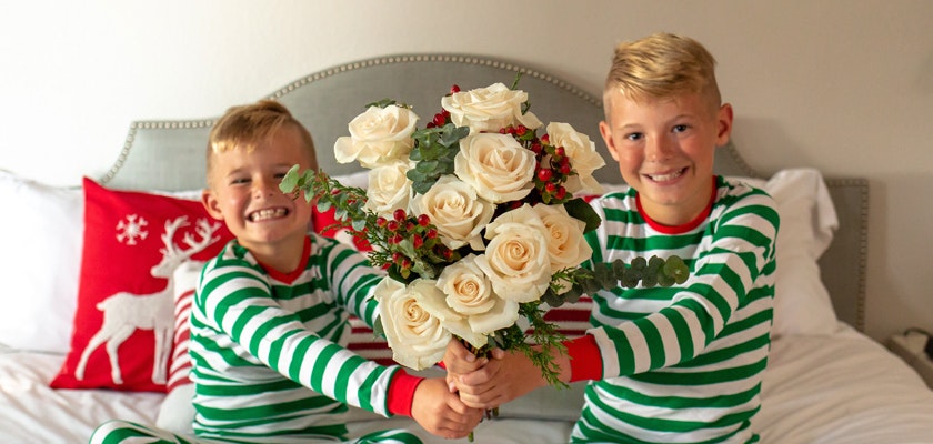 Two smiling boys in festive striped pajamas holding a beautiful bouquet of white roses and greenery.