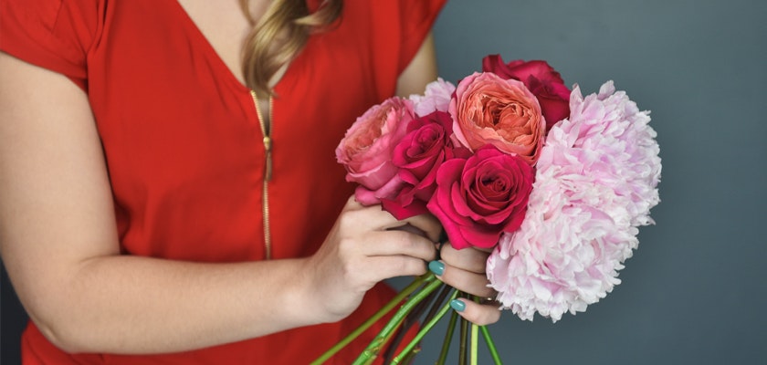 A vibrant bouquet featuring pink roses and peonies, held by a woman in a stylish red top.