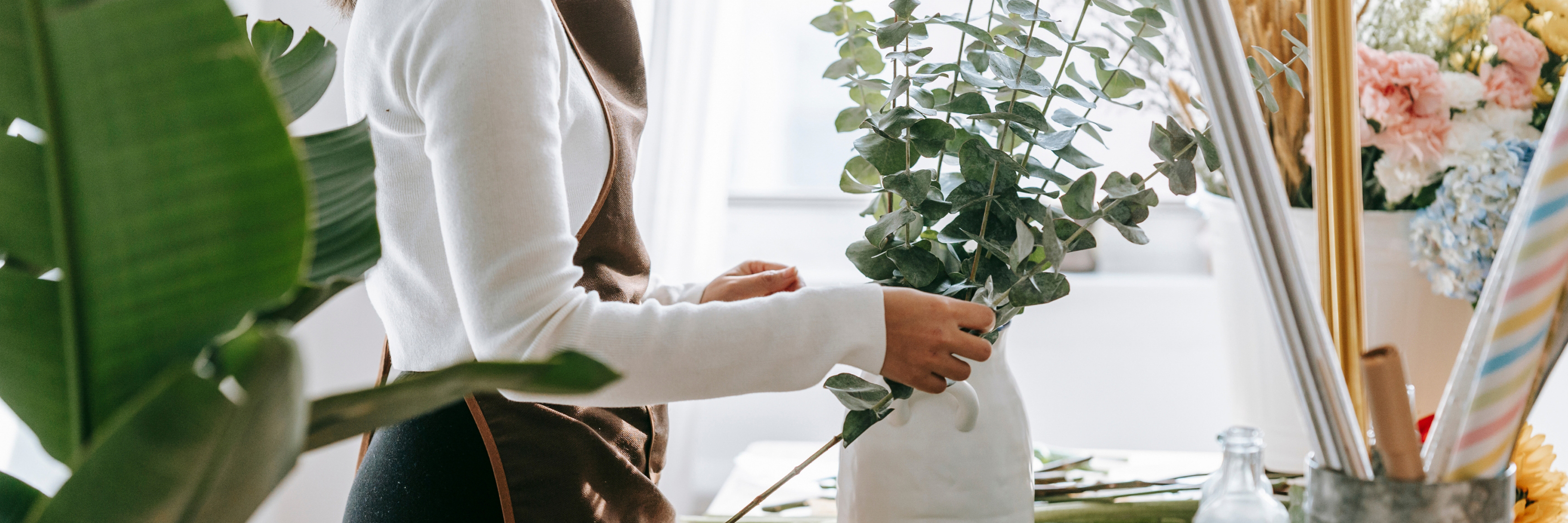 A florist arranging eucalyptus in a stylish vase, surrounded by vibrant flowers and greenery.