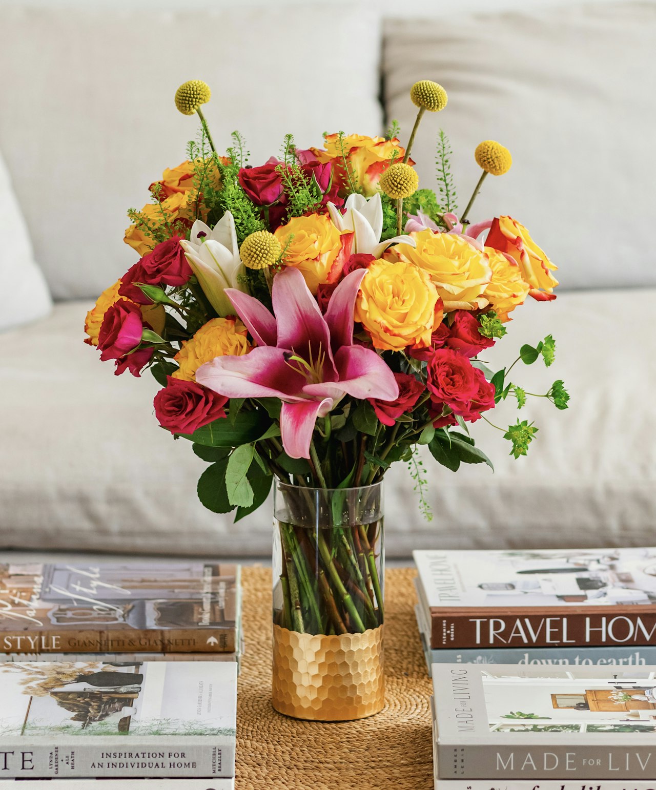 Vibrant floral arrangement with yellow roses, lilies, and seasonal blooms in a glass vase.