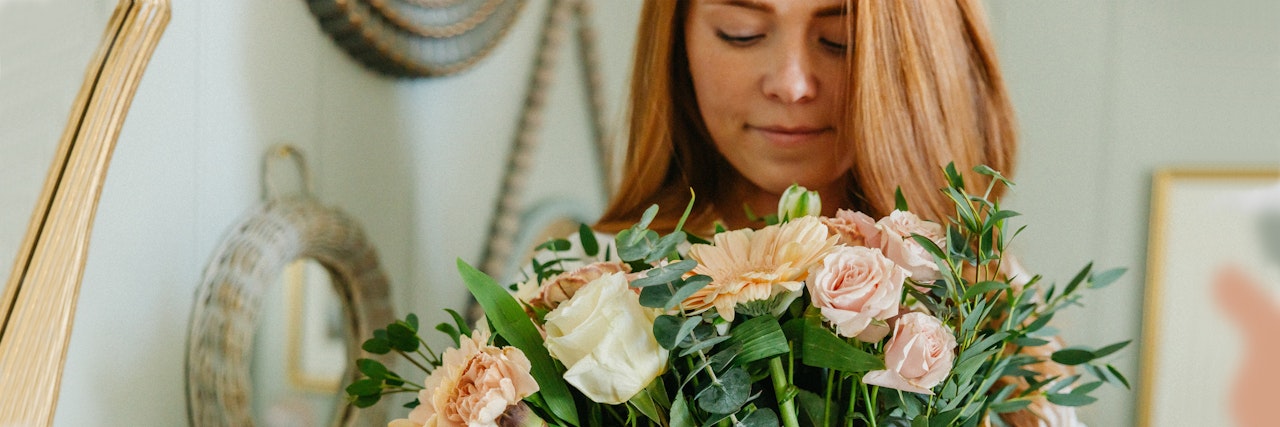 A woman holding a lush bouquet of soft pink and cream flowers with greenery accents.