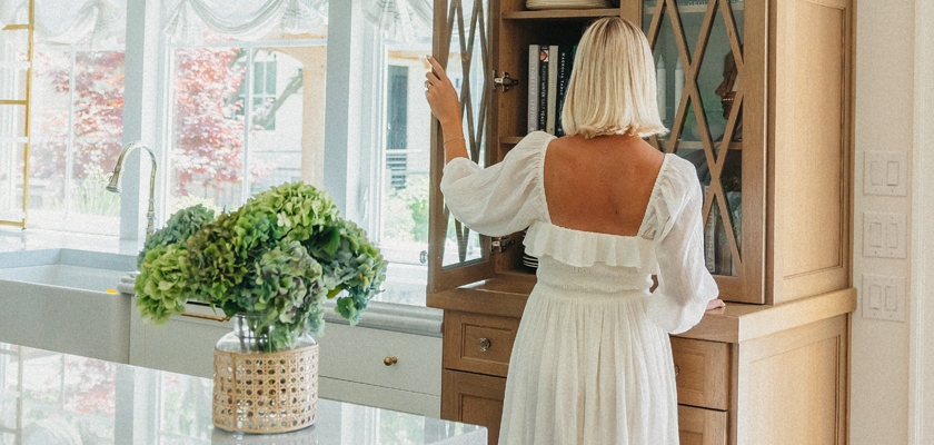 A woman in a white dress exploring a stylish kitchen with a vase of green hydrangeas.