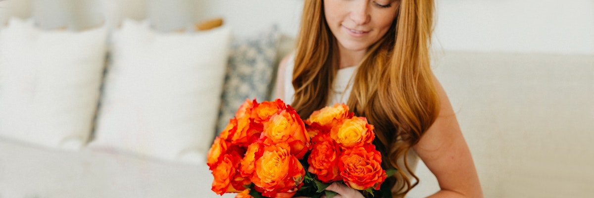 A woman with long hair holding a vibrant bouquet of orange roses, radiating warmth and beauty.