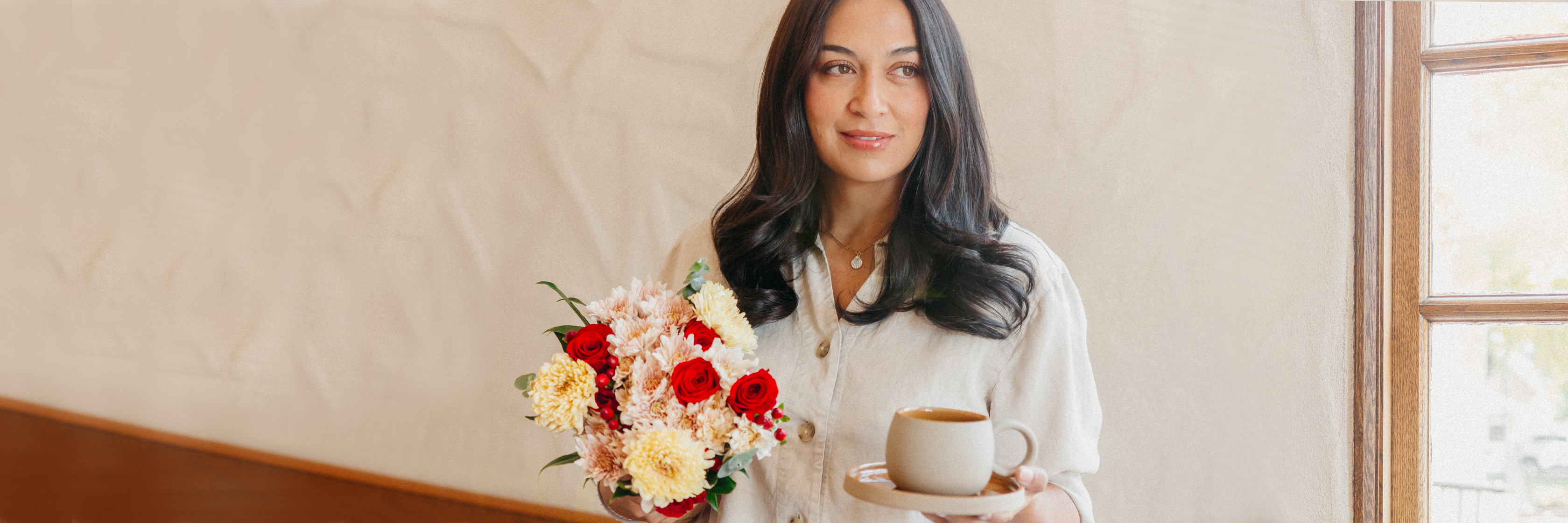 A woman holding a vibrant bouquet of flowers and a cup of coffee, radiating warmth and joy.