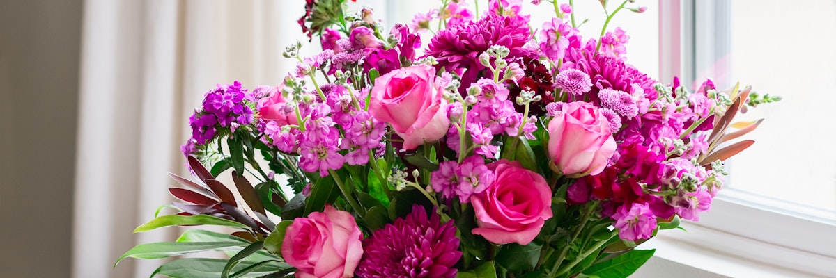 Vibrant pink floral arrangement featuring roses and blossoms by a sunny window.