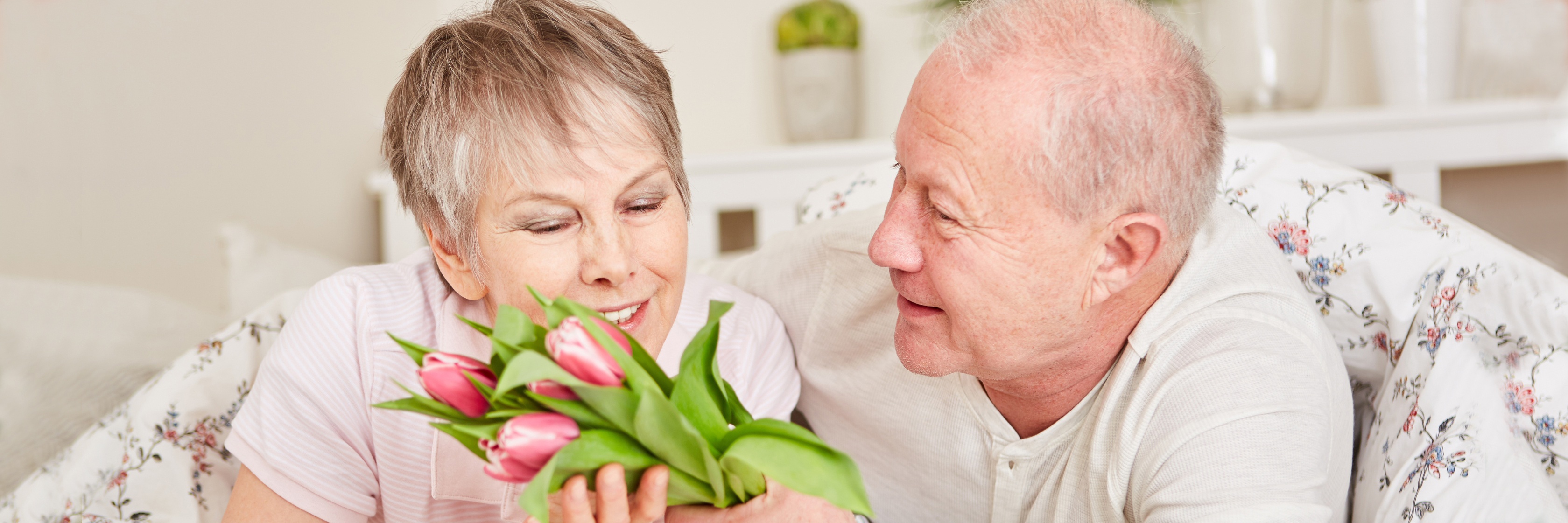 Cheerful elderly couple sharing a tender moment with pink tulips in hand, celebrating love.