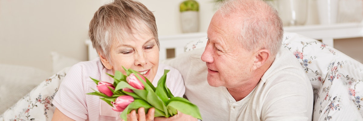 Cheerful elderly couple sharing a tender moment with pink tulips in hand, celebrating love.