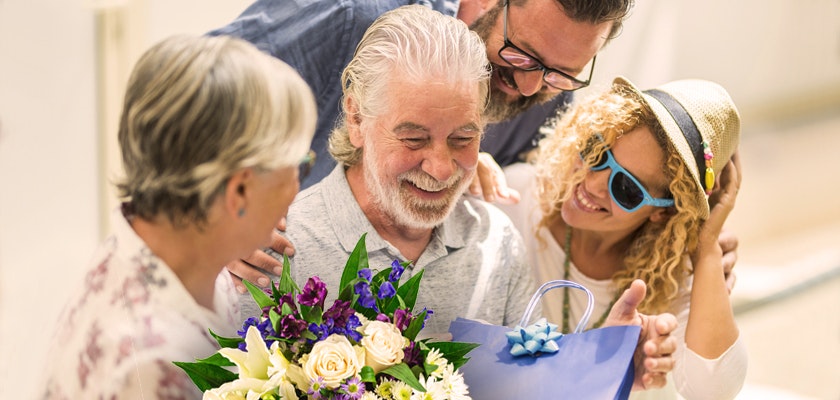 A joyful family celebration featuring a smiling older man receiving a vibrant flower bouquet.