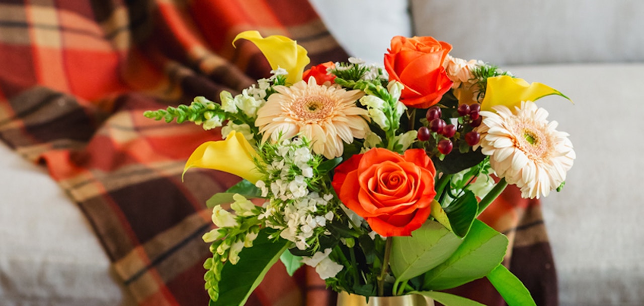 Vibrant floral arrangement featuring orange roses, gerbera daisies, and calla lilies in a stylish vase.