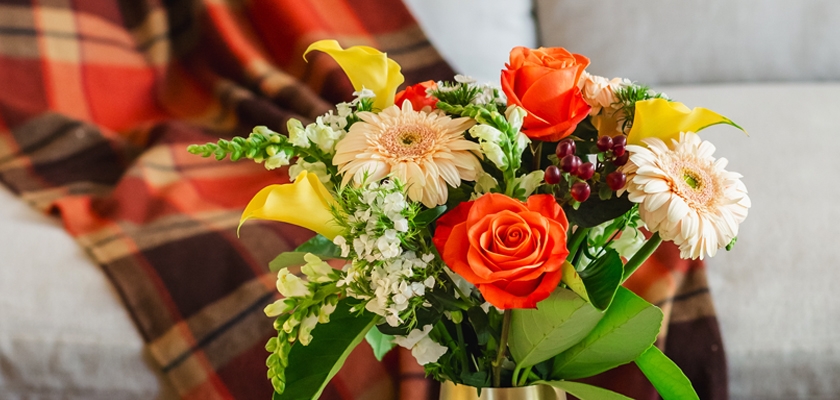 Bright floral arrangement featuring orange roses, yellow calla lilies, and cheerful gerberas.