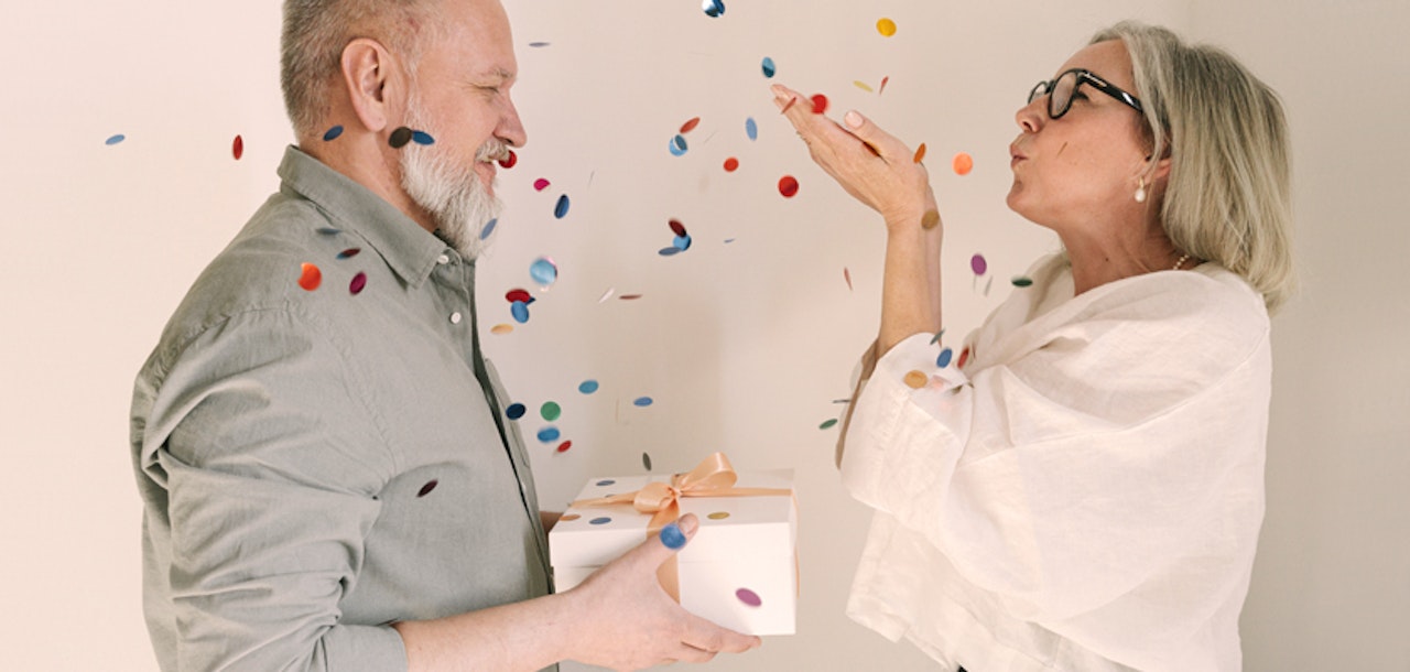 Joyful couple celebrating a special occasion with confetti and a gift, radiating happiness and love.