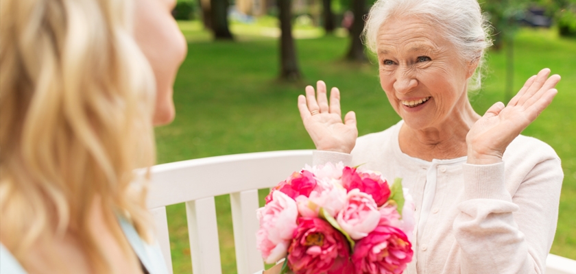 A joyful elderly woman receives a vibrant bouquet of pink flowers in a sunny park setting.