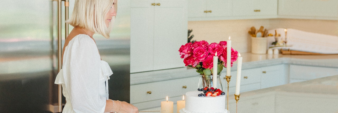 A woman in a white dress elegantly prepares to cut a cake adorned with fresh berries and flowers.