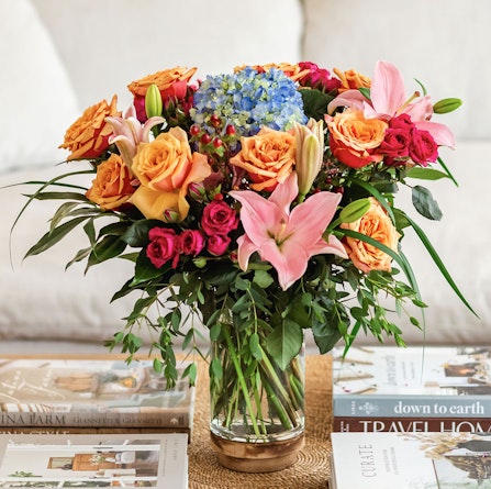 Vibrant floral arrangement featuring roses, hydrangeas, and lilies in a chic glass vase.