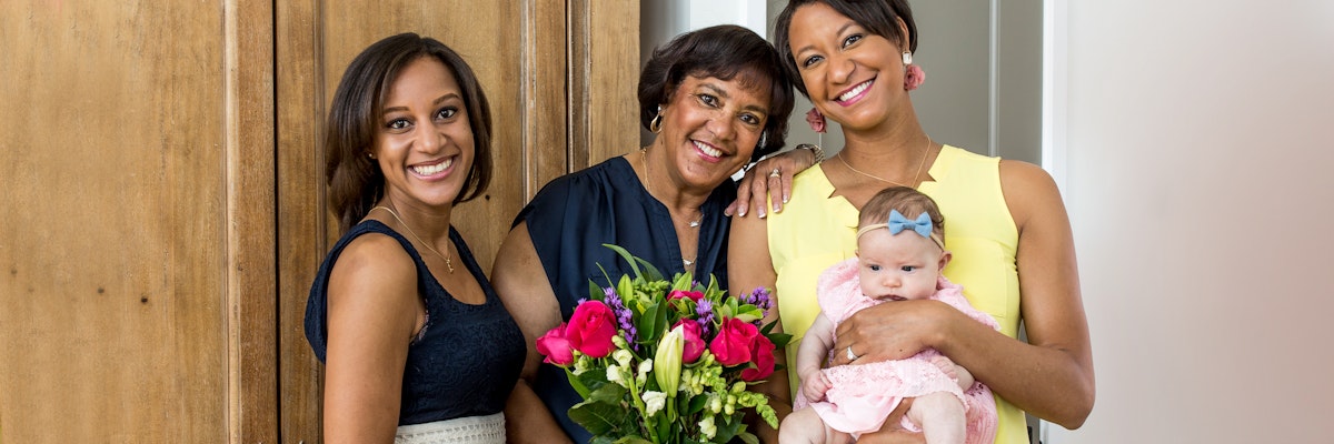 A joyful family portrait featuring three women holding a vibrant floral bouquet and a baby.
