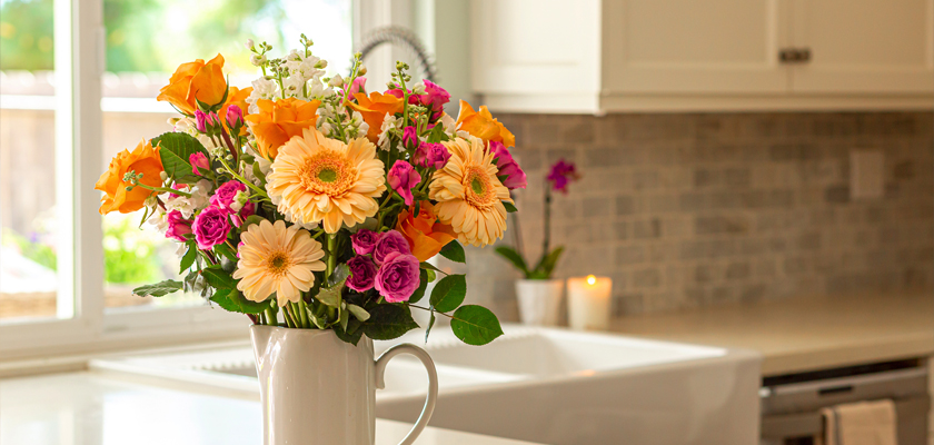 Vibrant floral arrangement featuring orange roses and pink gerberas in a bright kitchen setting.