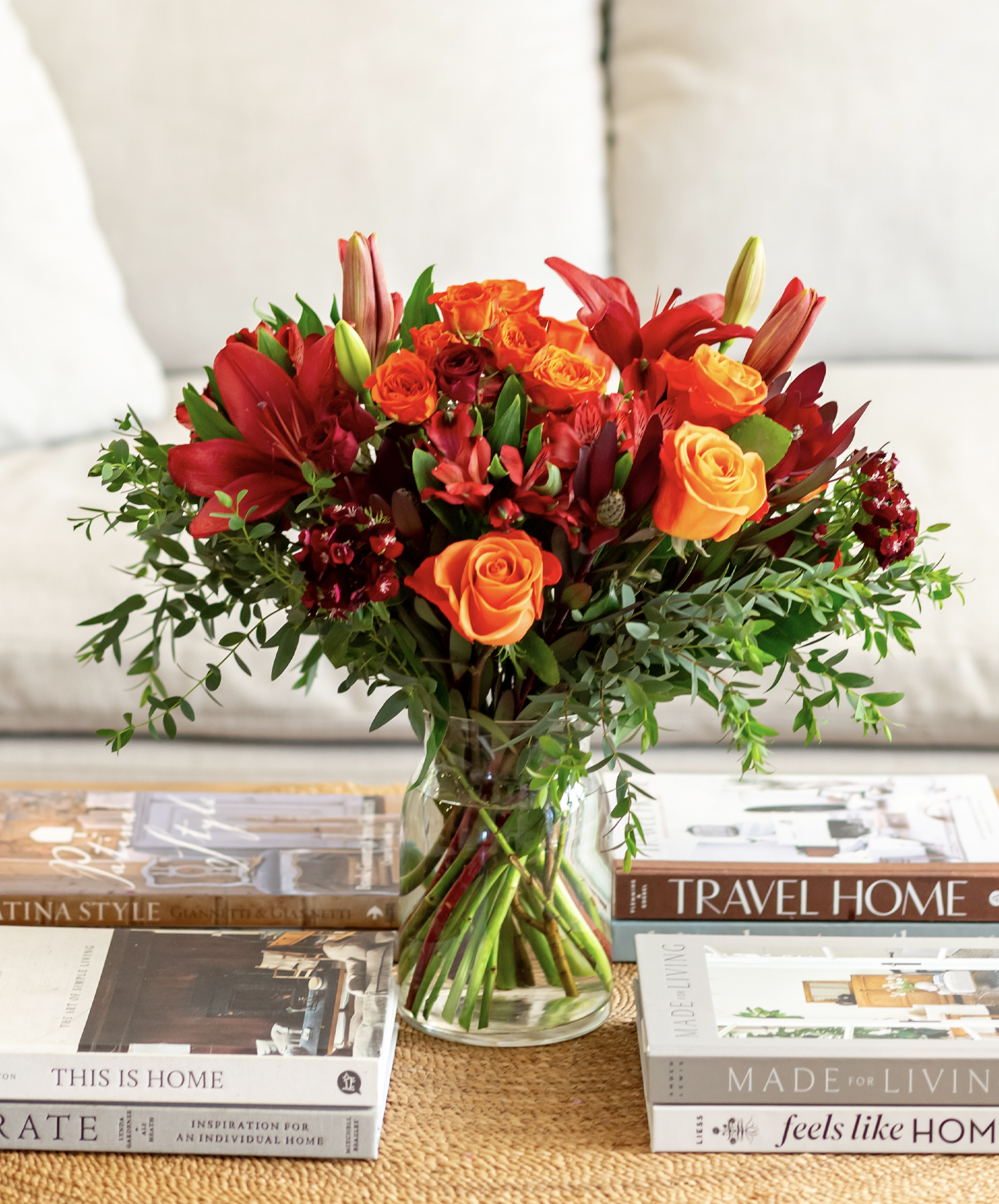 Vibrant floral arrangement featuring red roses, orange lilies, and lush greenery in a clear vase.