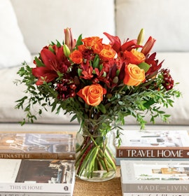 Vibrant floral arrangement featuring red roses, orange lilies, and lush greenery in a clear vase.
