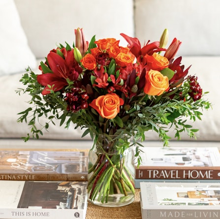 Vibrant floral arrangement featuring red roses, orange lilies, and lush greenery in a clear vase.