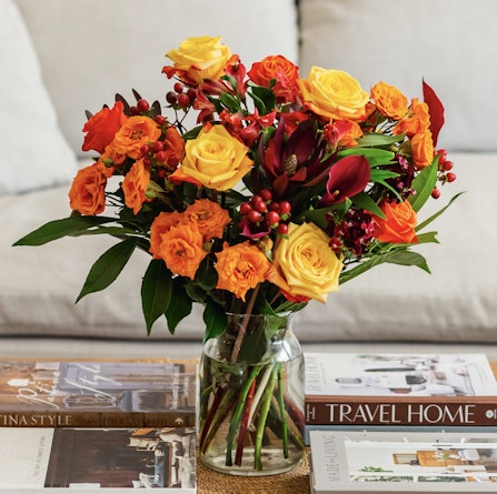 Vibrant bouquet featuring yellow and orange roses with greenery, enhancing a cozy living space.