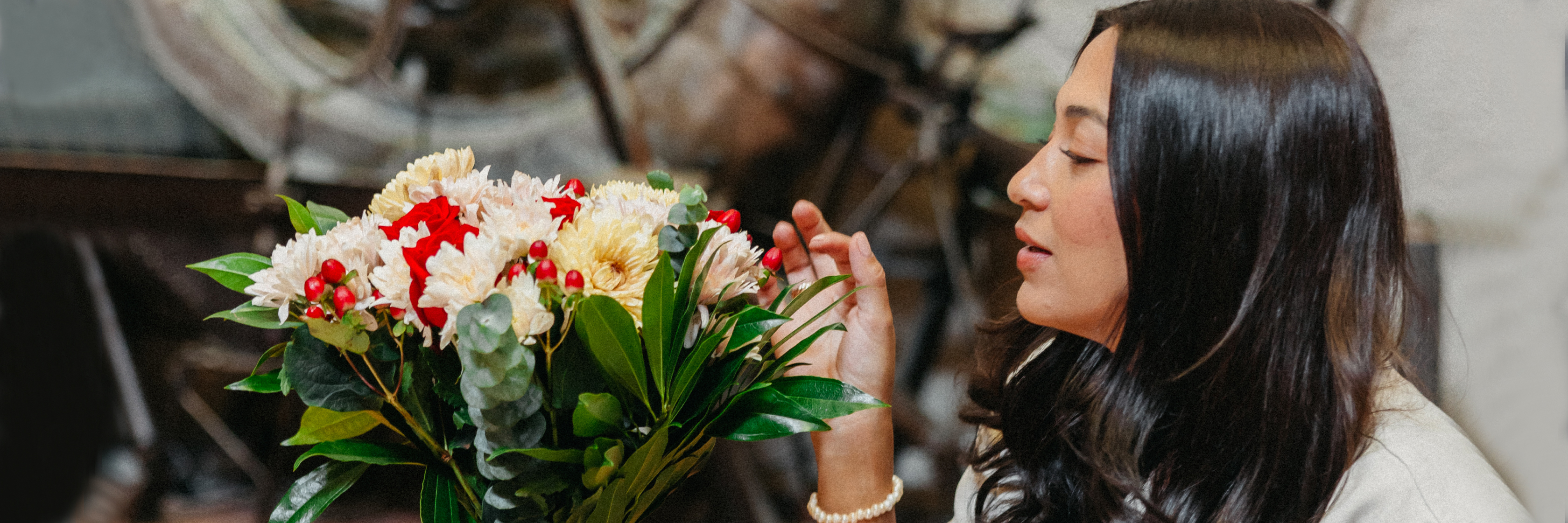 A woman admires a vibrant bouquet featuring red and white flowers, surrounded by lush green foliage.
