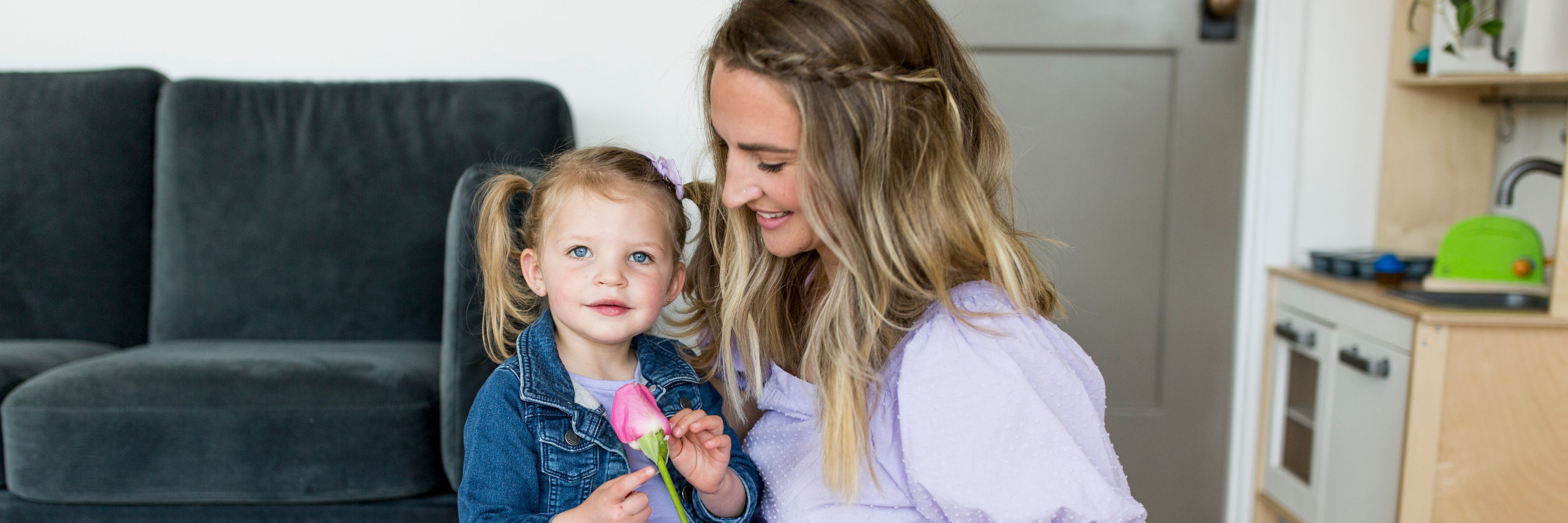 A joyful mother and daughter enjoying a moment together, with the little girl holding a pink flower.