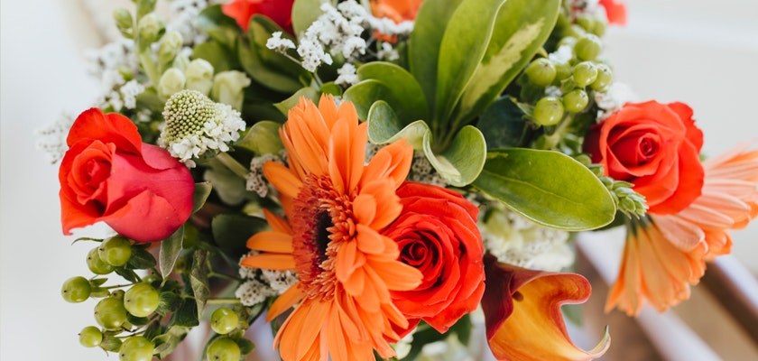 Vibrant floral arrangement featuring orange gerberas, red roses, and lush greenery.