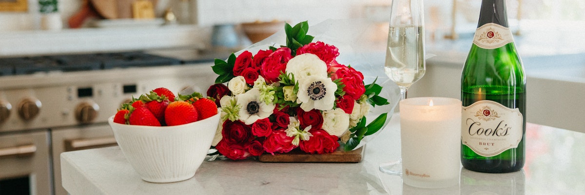 Vibrant bouquet of red and white flowers beside fresh strawberries and sparkling wine.