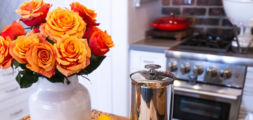 Vibrant orange and yellow roses in a white vase brighten a modern kitchen, adding charm.