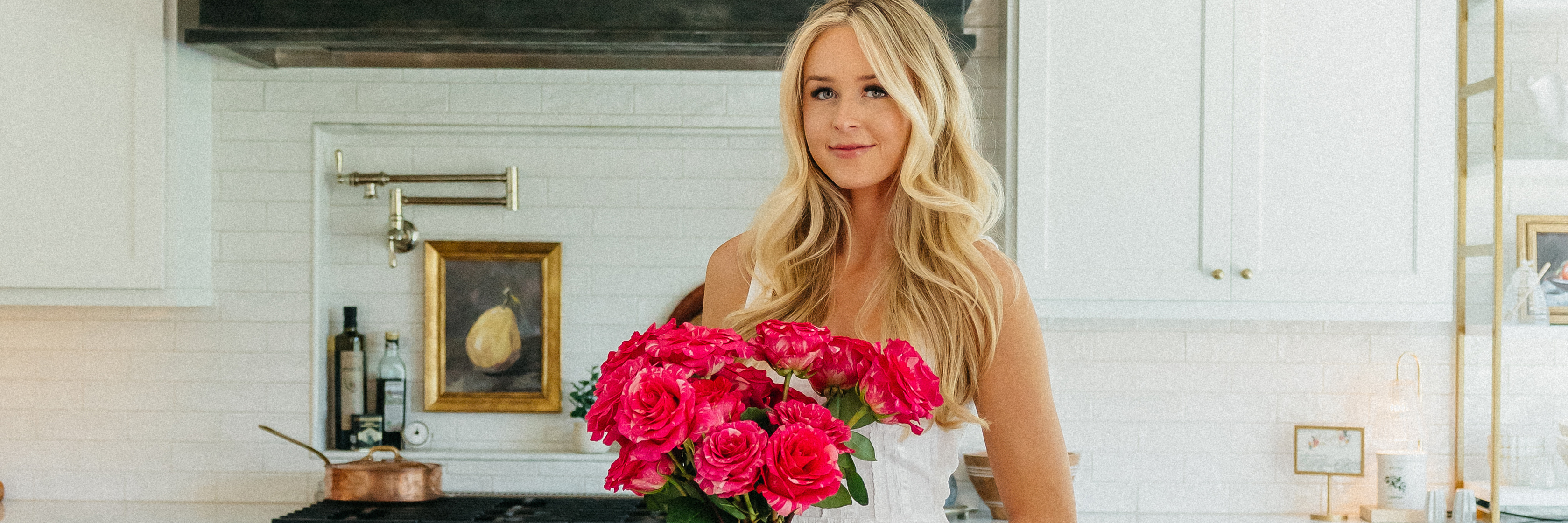 A young woman holds a vibrant bouquet of pink roses in a stylish kitchen, showcasing floral beauty.