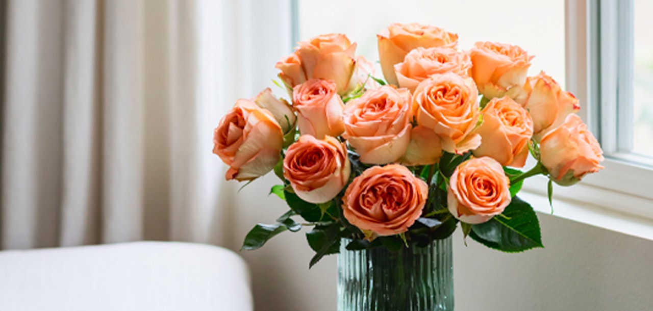 Vibrant bouquet of peach roses in a stylish glass vase, brightening up the room with elegance.