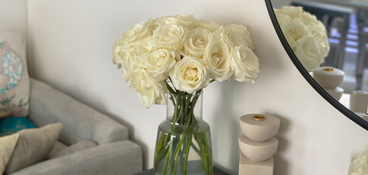 Elegant white roses in a glass vase, complemented by a modern living room decor featuring a mirror.