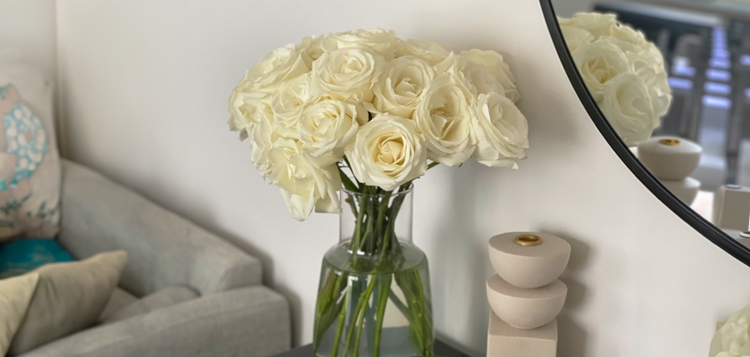 Elegant white roses in a glass vase, complemented by a modern living room decor featuring a mirror.