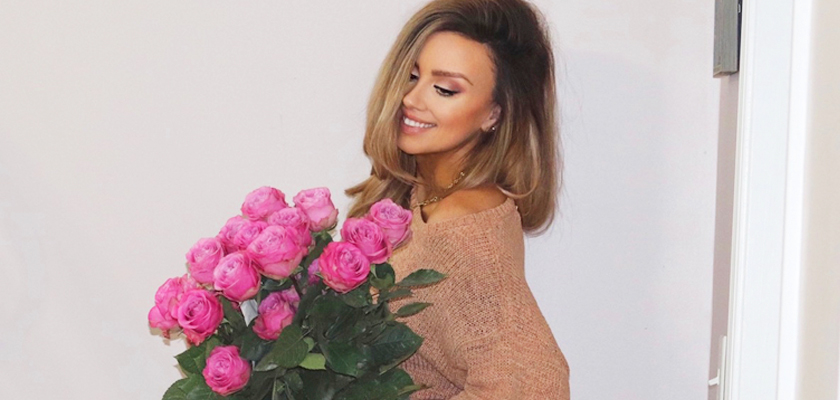Woman smiling while holding a large bouquet of vibrant pink roses against a light background.