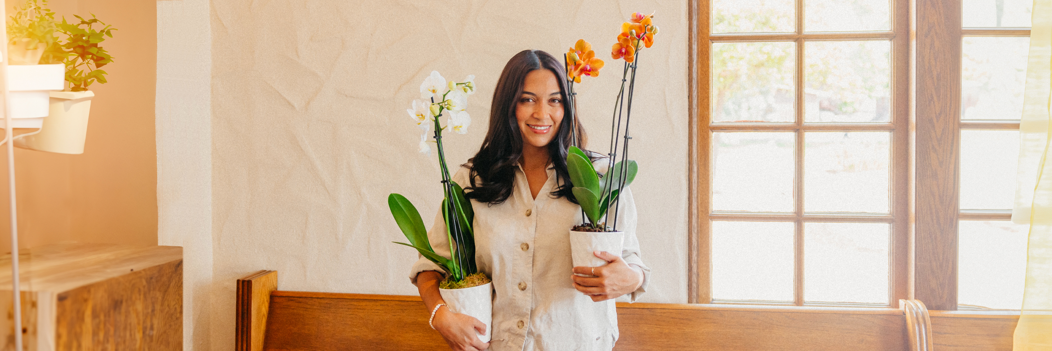 A woman holding two vibrant potted orchid plants, smiling in a bright indoor setting.