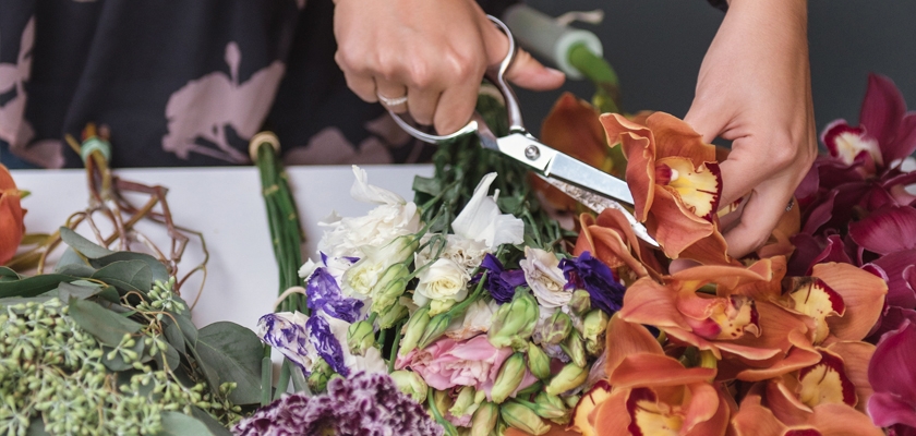 A florist expertly arranging a vibrant mix of colorful flowers with scissors for a stunning bouquet.