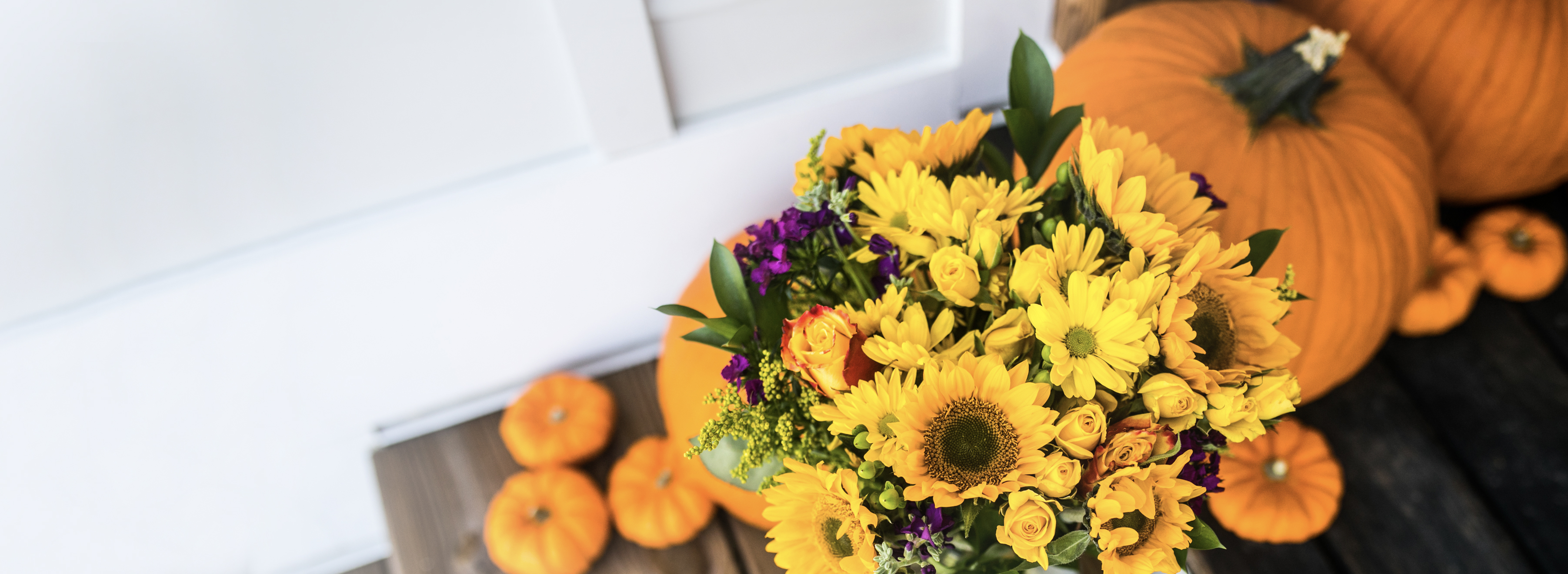 Vibrant fall bouquet of sunflowers and colorful blooms with pumpkins in the background.