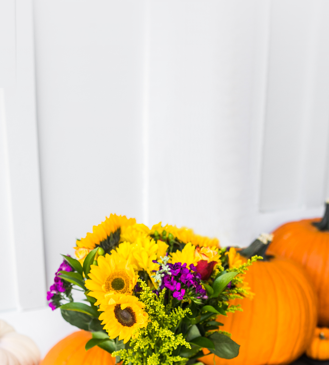 Vibrant sunflower bouquet with purple accents, decorated alongside bright pumpkins for fall.