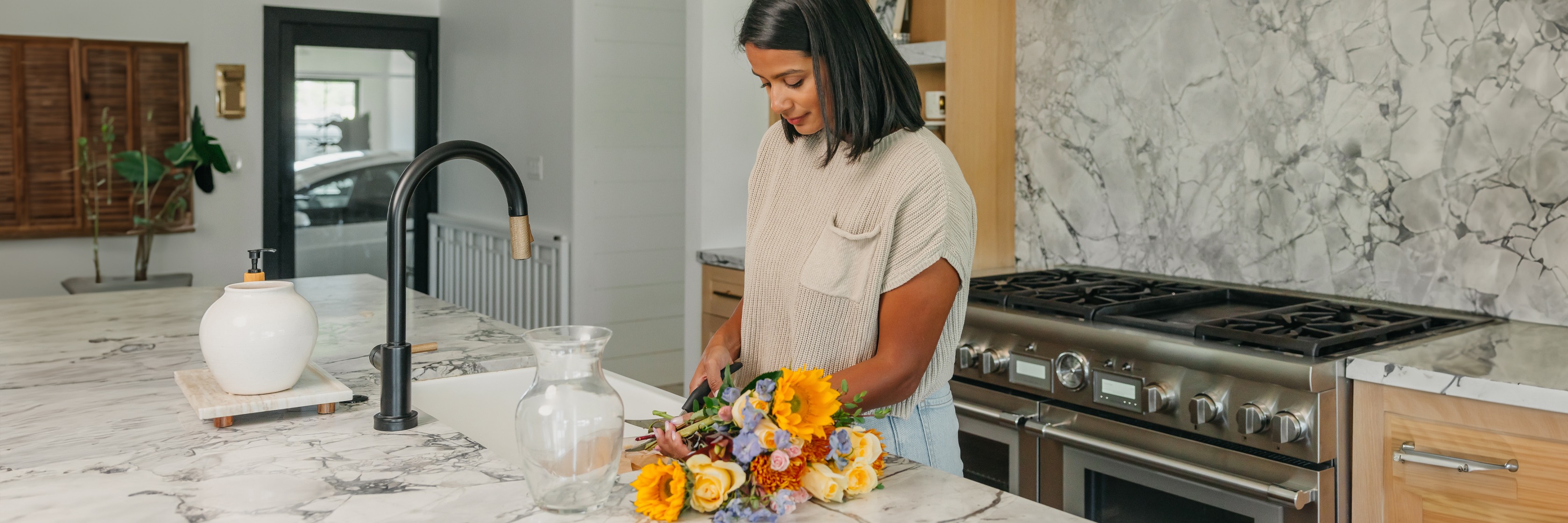 A woman arranging a vibrant bouquet of flowers in a modern kitchen with marble countertops.