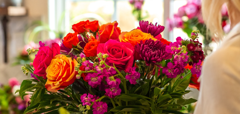 Vibrant floral arrangement featuring bold red and orange roses surrounded by rich purple blooms.