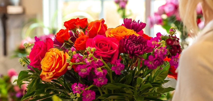 Vibrant floral arrangement featuring bold red and orange roses surrounded by rich purple blooms.