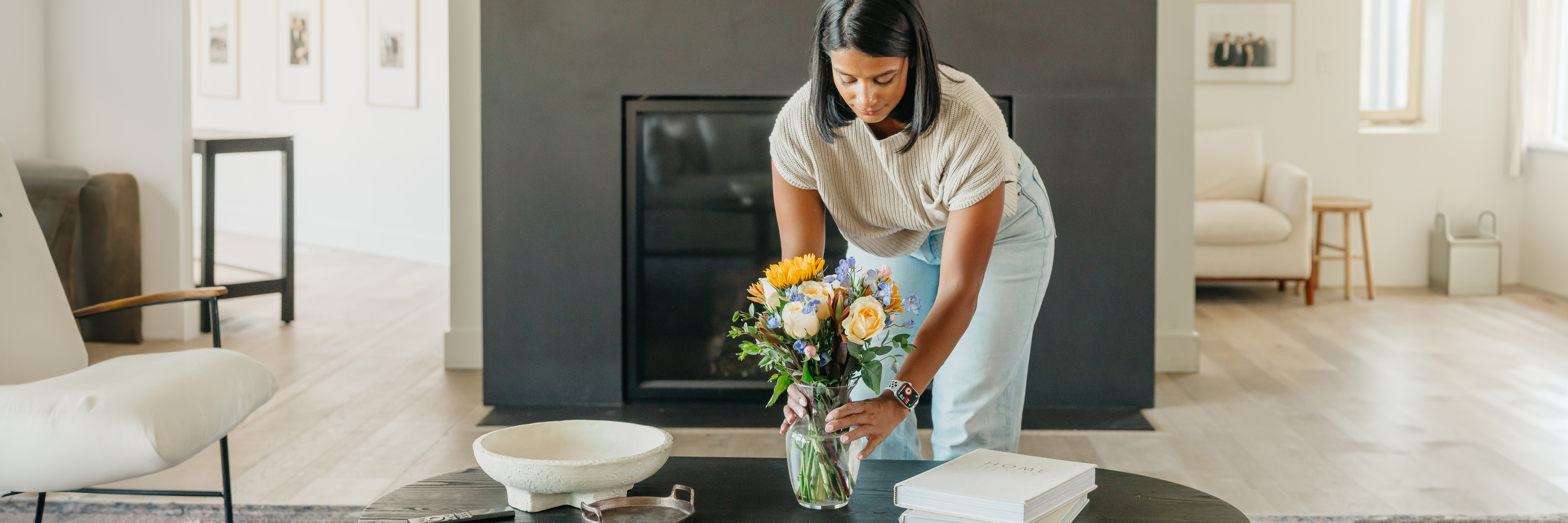 A woman arranging a colorful floral bouquet on a sleek coffee table in a modern living room.