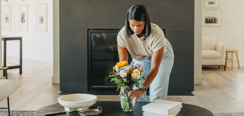 Woman arranging a floral bouquet with bright flowers in a stylish living room.