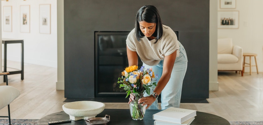 Woman arranging a floral bouquet with bright flowers in a stylish living room.