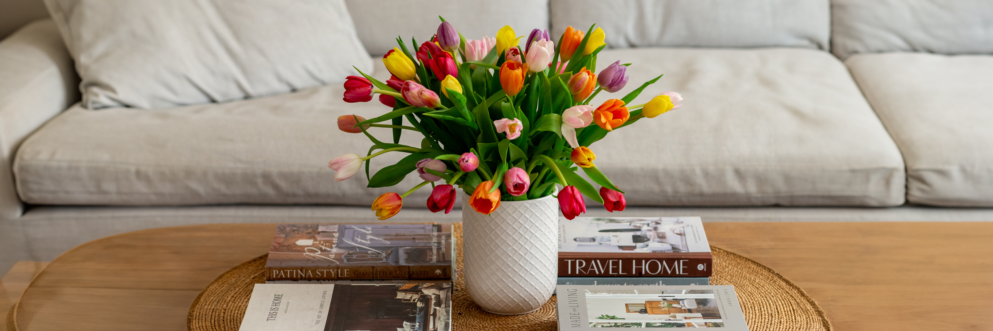 A vibrant bouquet of multicolored tulips in a stylish vase on a wooden coffee table.