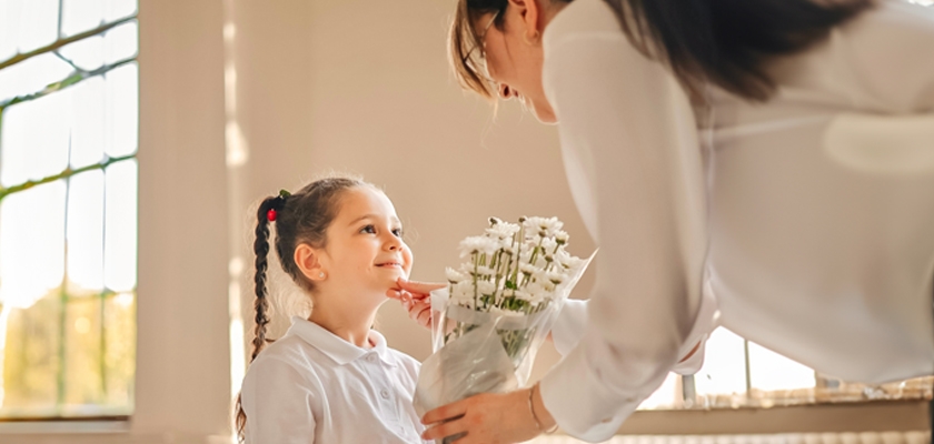 A heartwarming moment of a mother gifting a bouquet of white flowers to her smiling daughter.
