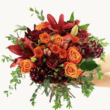 Vibrant bouquet of orange and red roses with lush greenery, perfect for celebrations and gifting.