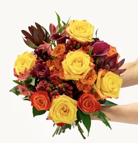Vibrant bouquet of yellow and orange roses mixed with lush greenery, perfect for celebrations.