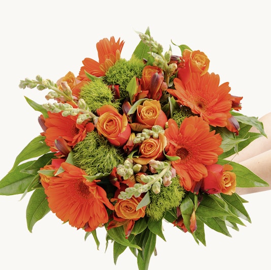 Vibrant orange flower bouquet featuring roses, gerberas, and lush greenery.